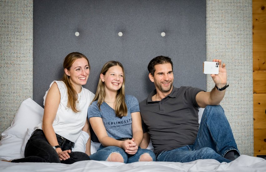 Familie sitzt am Bett und macht ein Selfie mit dem Smartphone